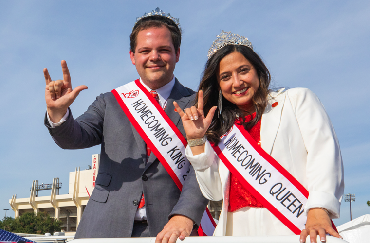 2023 Homecoming King and Queen wearing Homecoming Court sashes pose with UL Lafayette hand sign in front of Cajun Field
